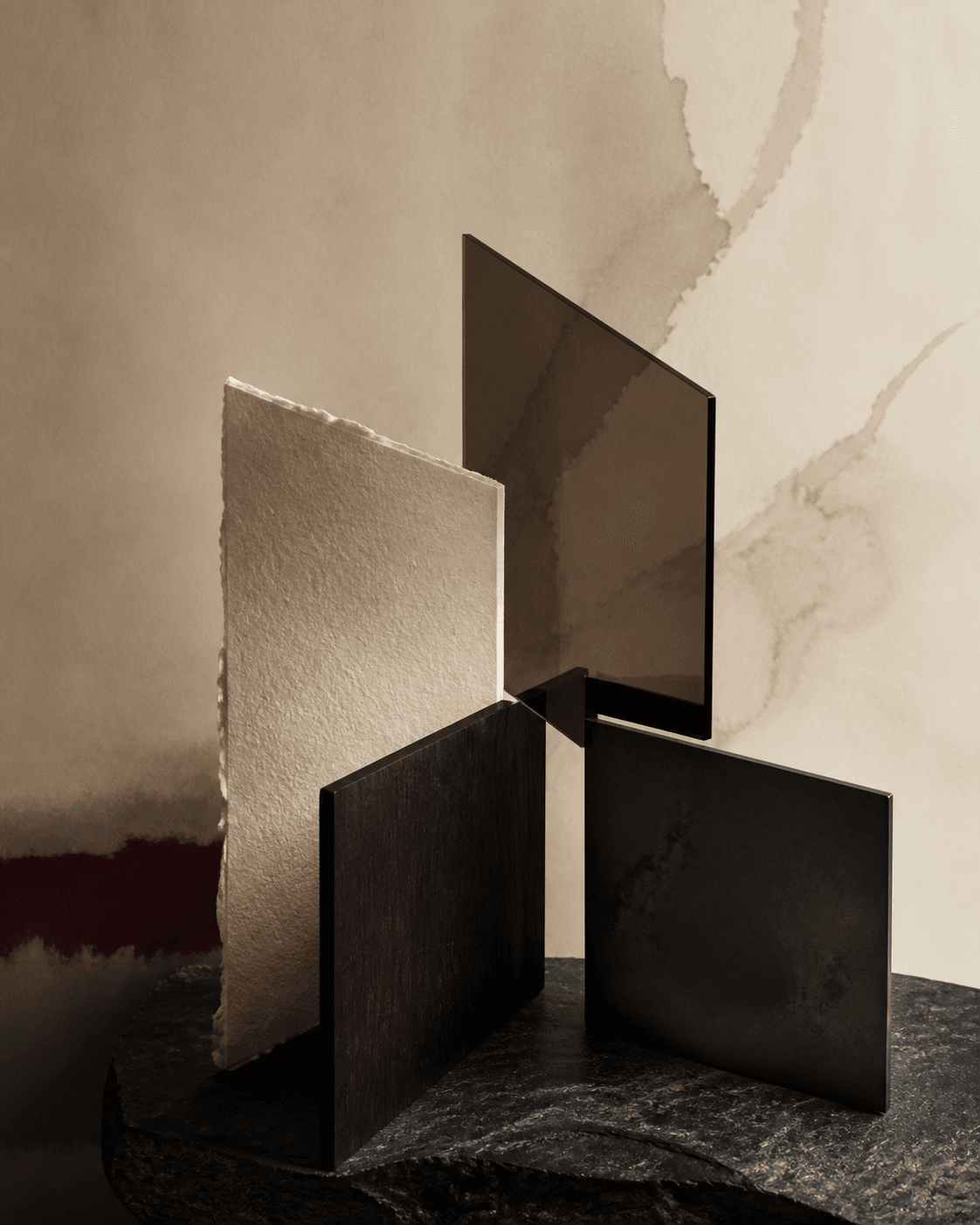 An editorial still life of folded vellum, stone, dark wood, and glass arranged as converging forms